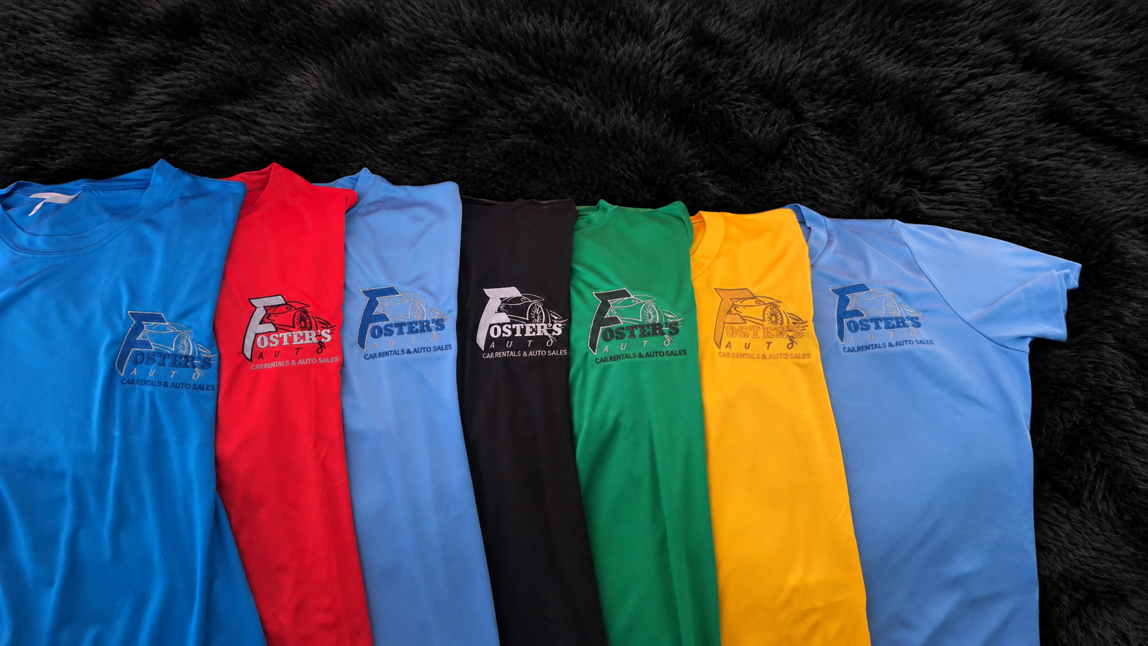 Seven colorful Foster's Auto embroidered shirts displayed on a black plush rug